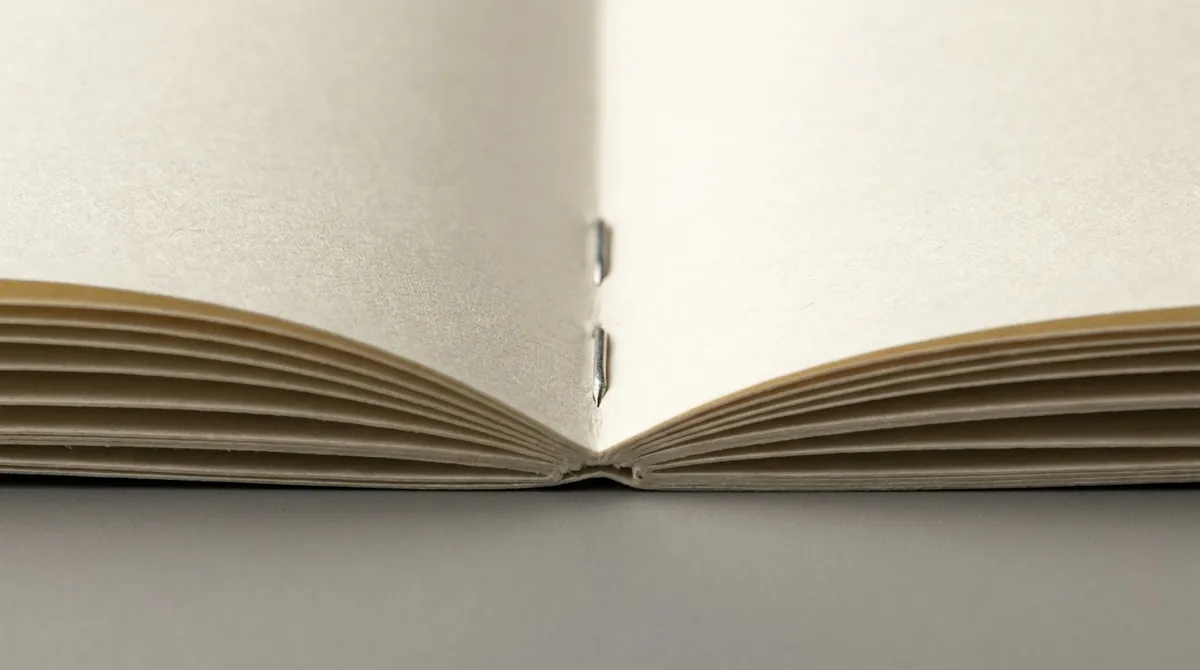 騎馬釘小冊子完全攤平,中央摺口兩枚銀色釘書釘清晰可見,兩邊書頁完全平放